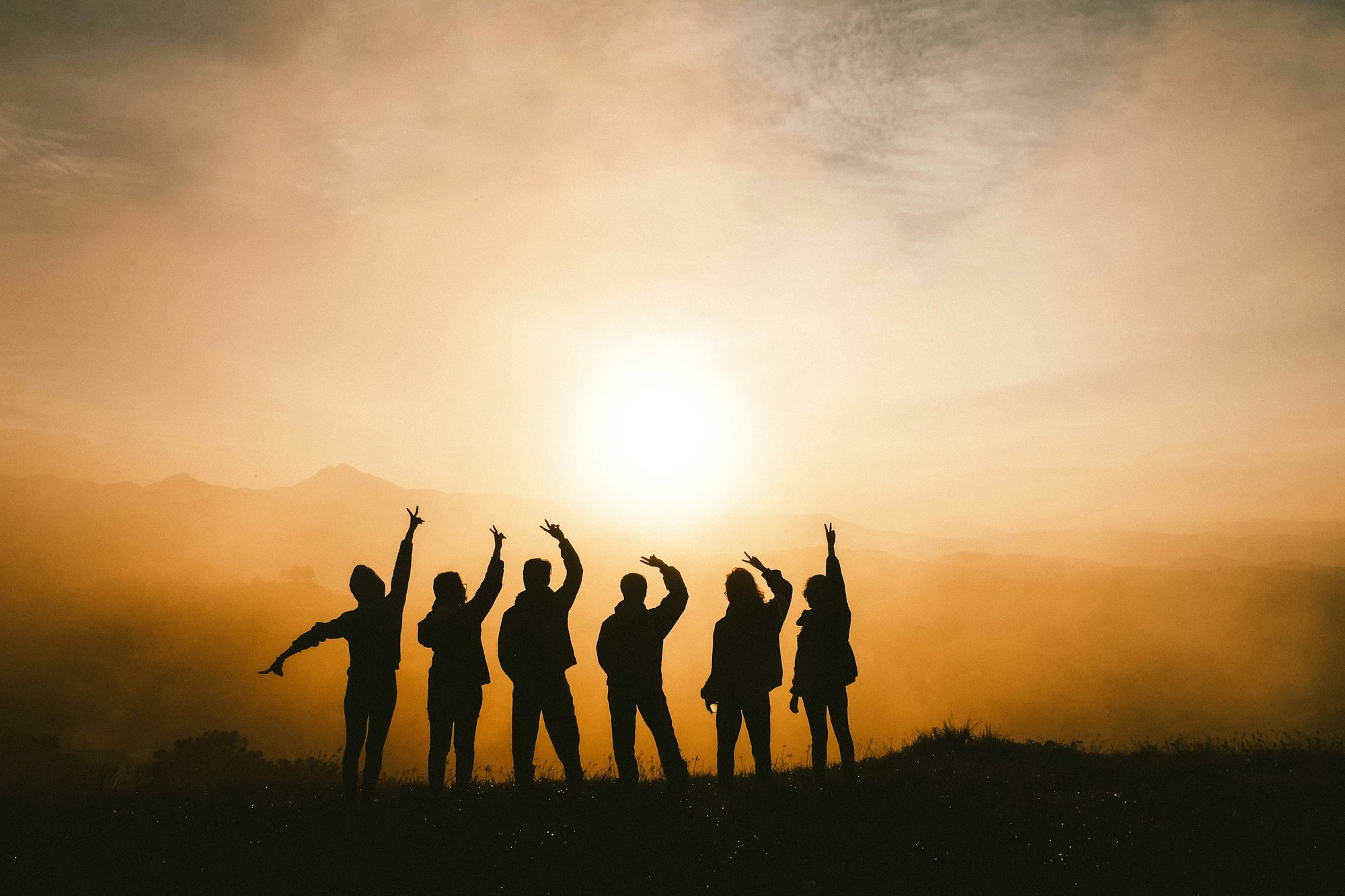 Silhouettes of friends raising their arms at sunset on a hill