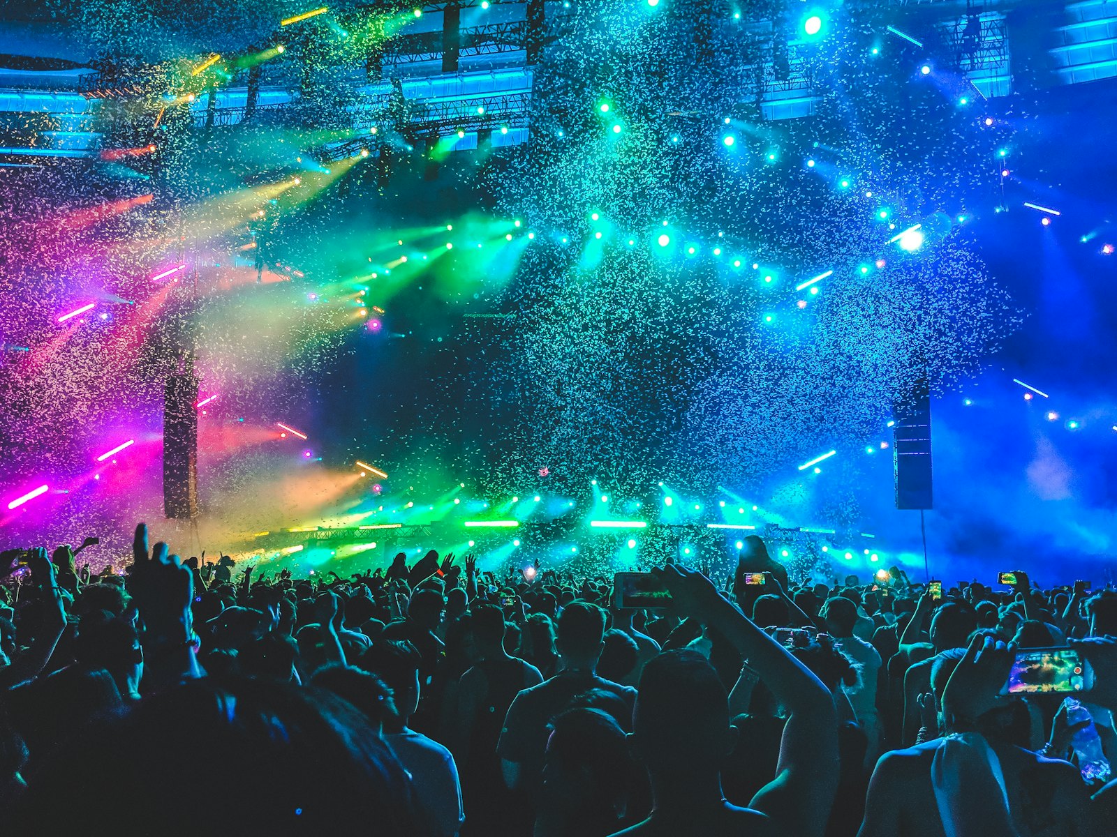 A stage washed in green and blue light with confetti falling over the crowd