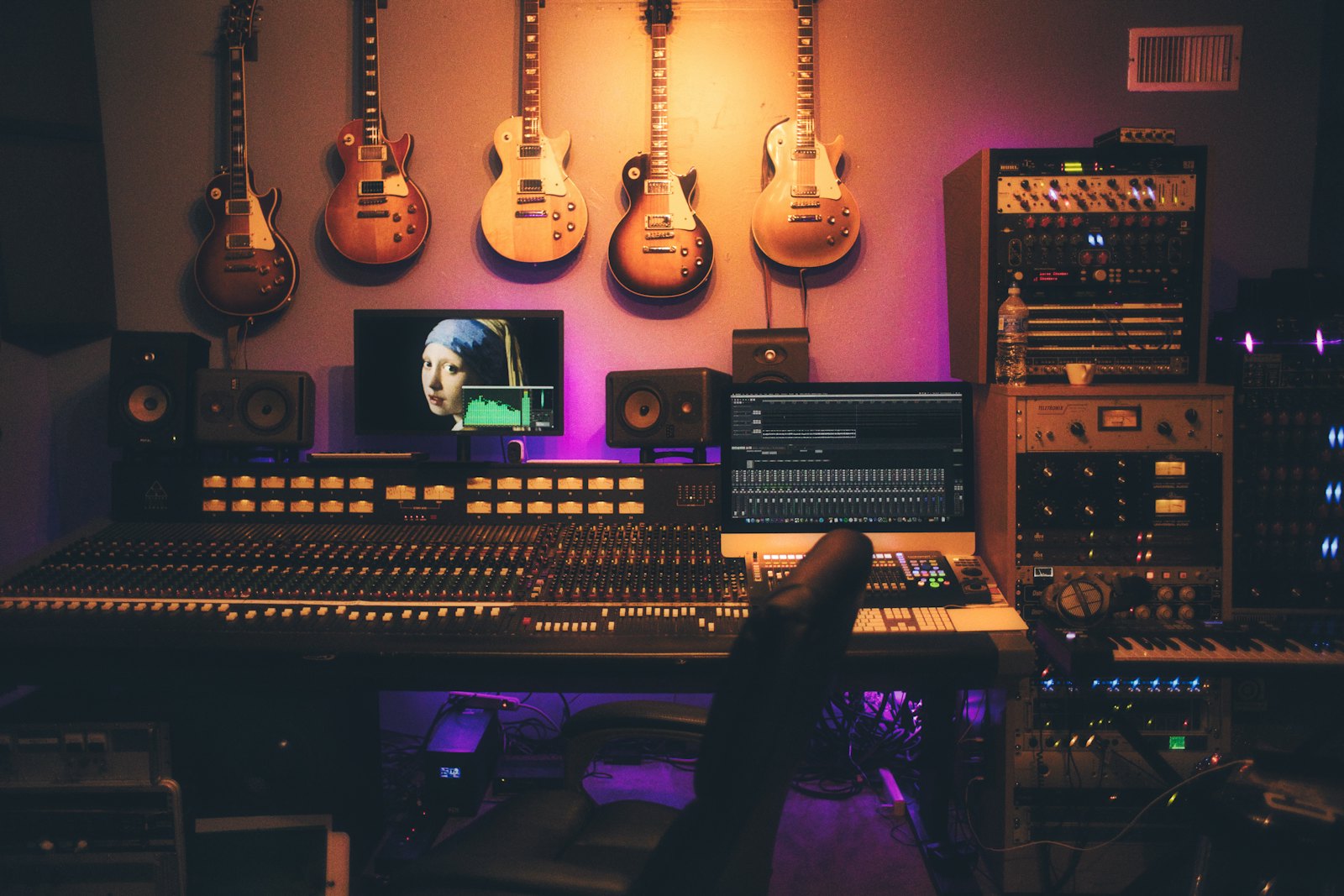 A studio mixing console with monitors and guitars on the wall